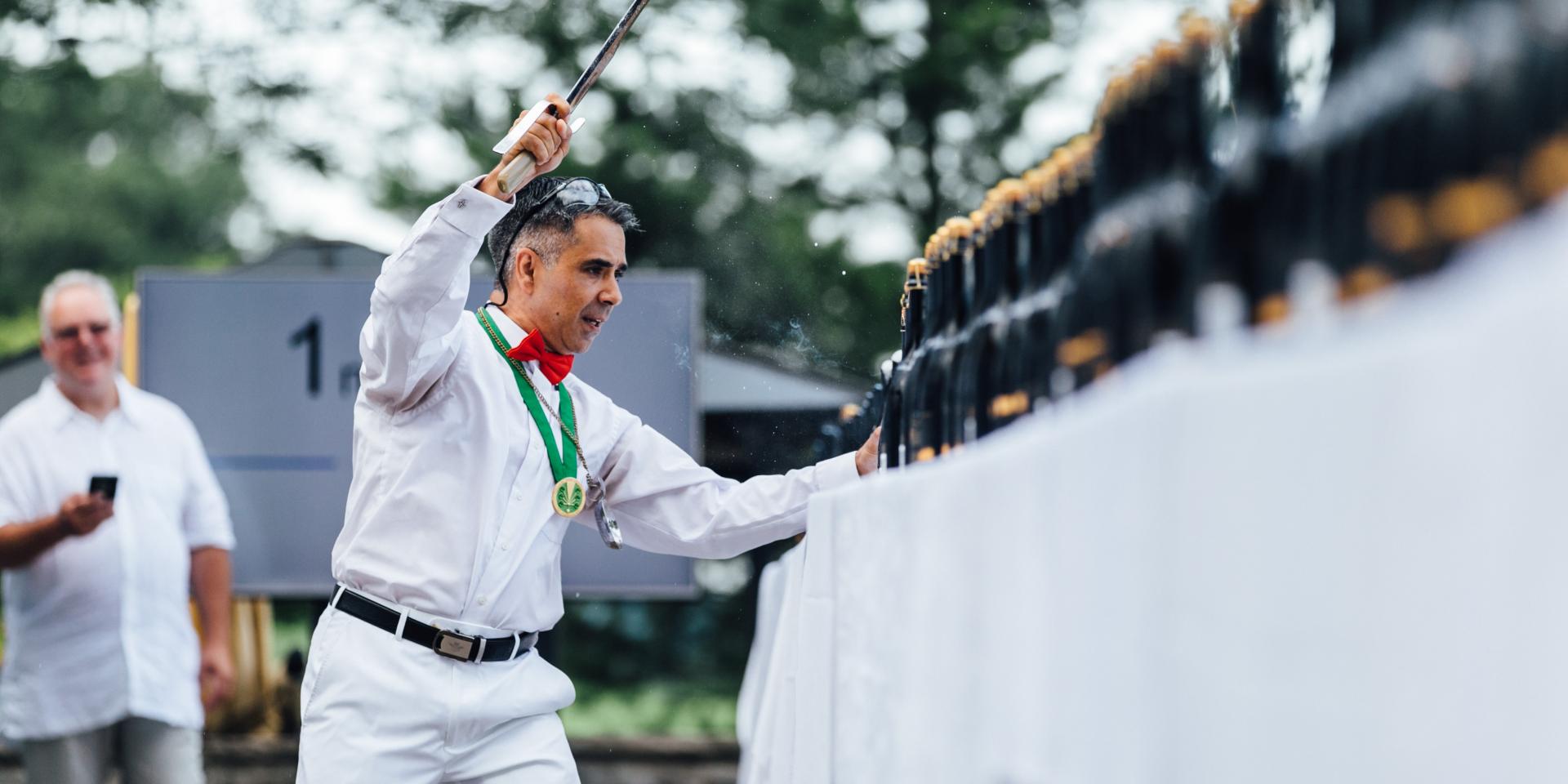 2017 Wine Event Sabering man standing in front of row of champagne bottles with saber raised in air