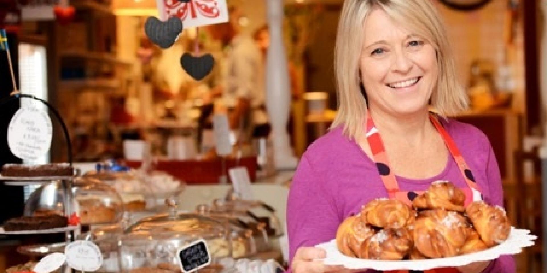 young blonde woman holding a plate of pastries with bakeshop in the background