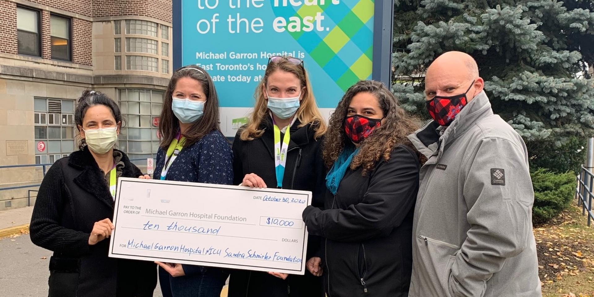 five people standing in front of the hospital holding a giant cheque 