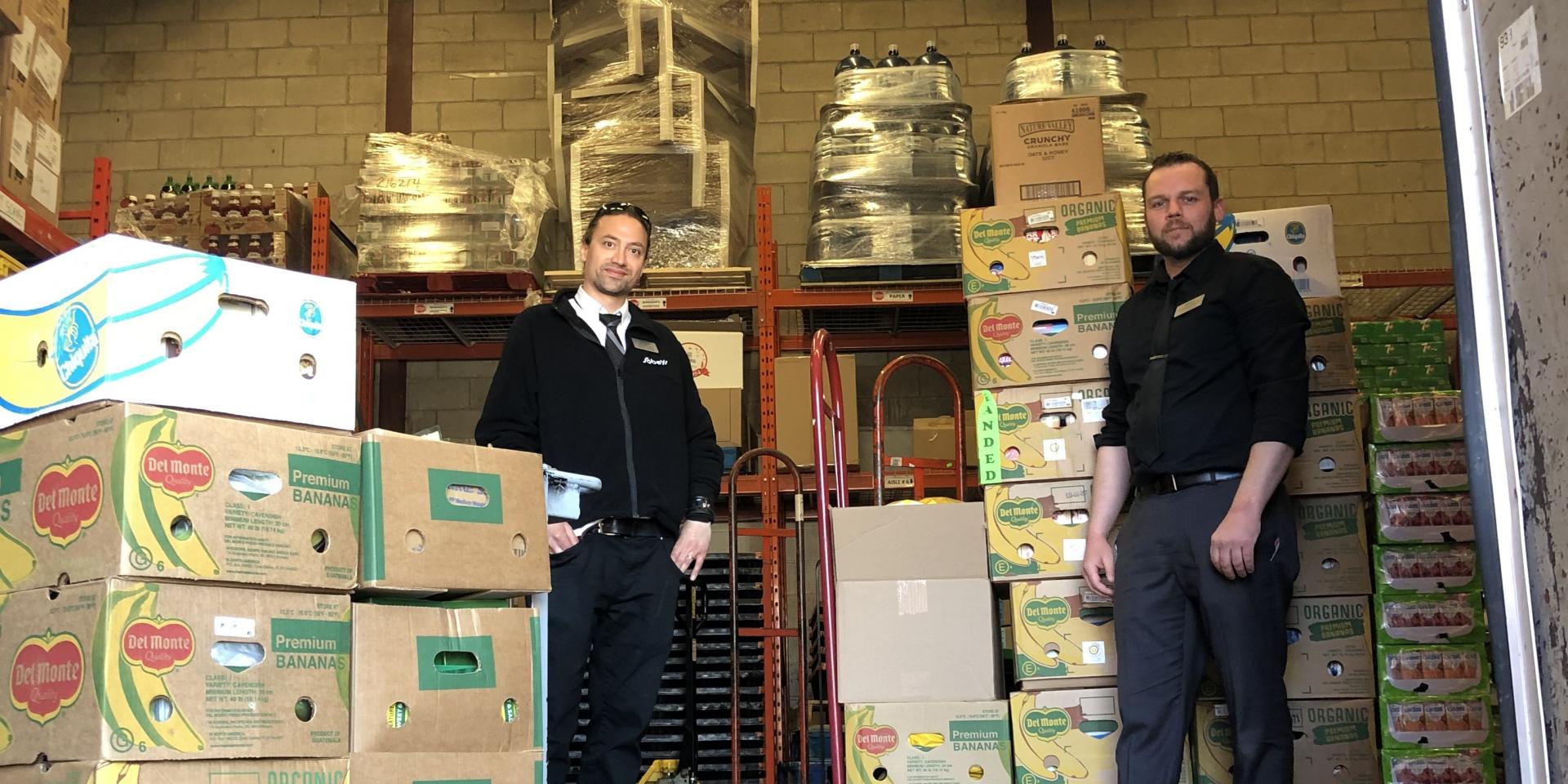 two men standing in back of truck with skids of boxes with food donations 