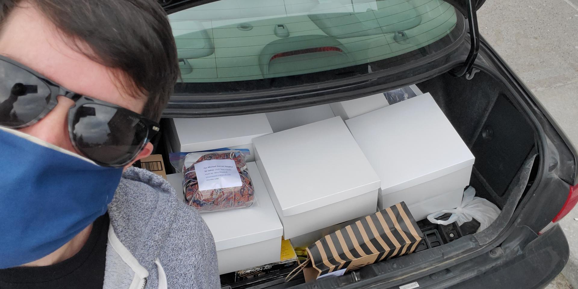 man wearing mask next to car trunk with boxes