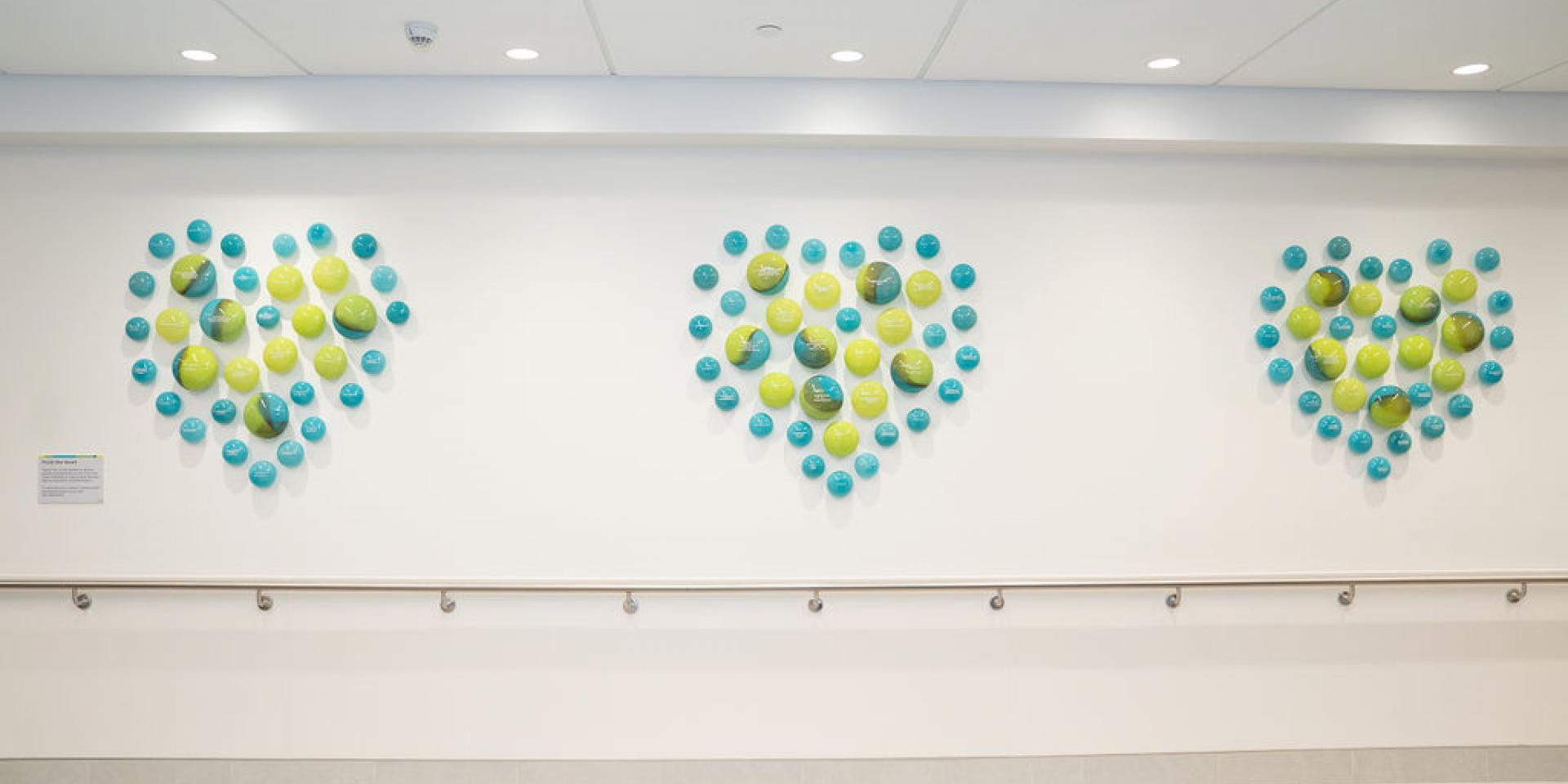 a wall with blue and green glass orbs making up three hearts on the wall, engraved with donor names. 