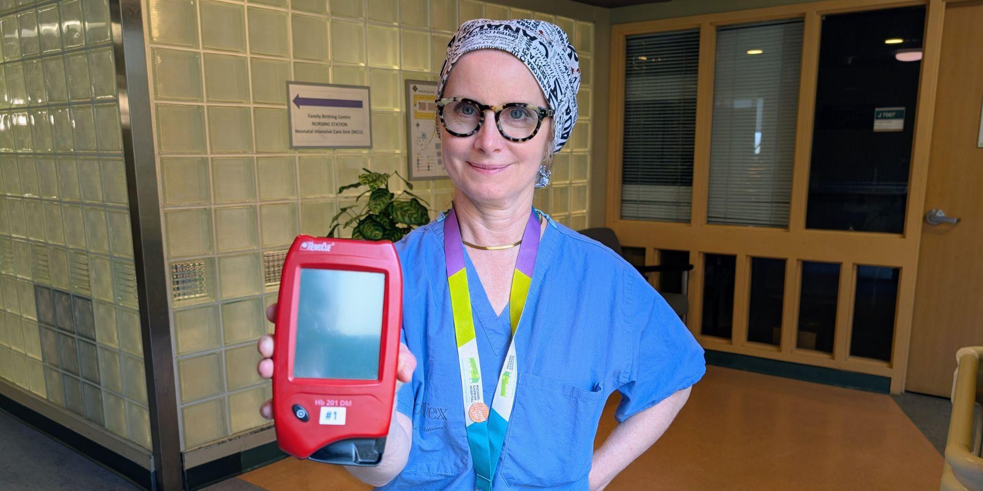 Dr. Elin Raymond, Chief of Obstetrics and Gynaecology and Medical Co-Director of Maternal, Newborn and Child Services, holds a red, palm-sized, HemoCue machine. It allows fast and accurate assessment of blood loss.