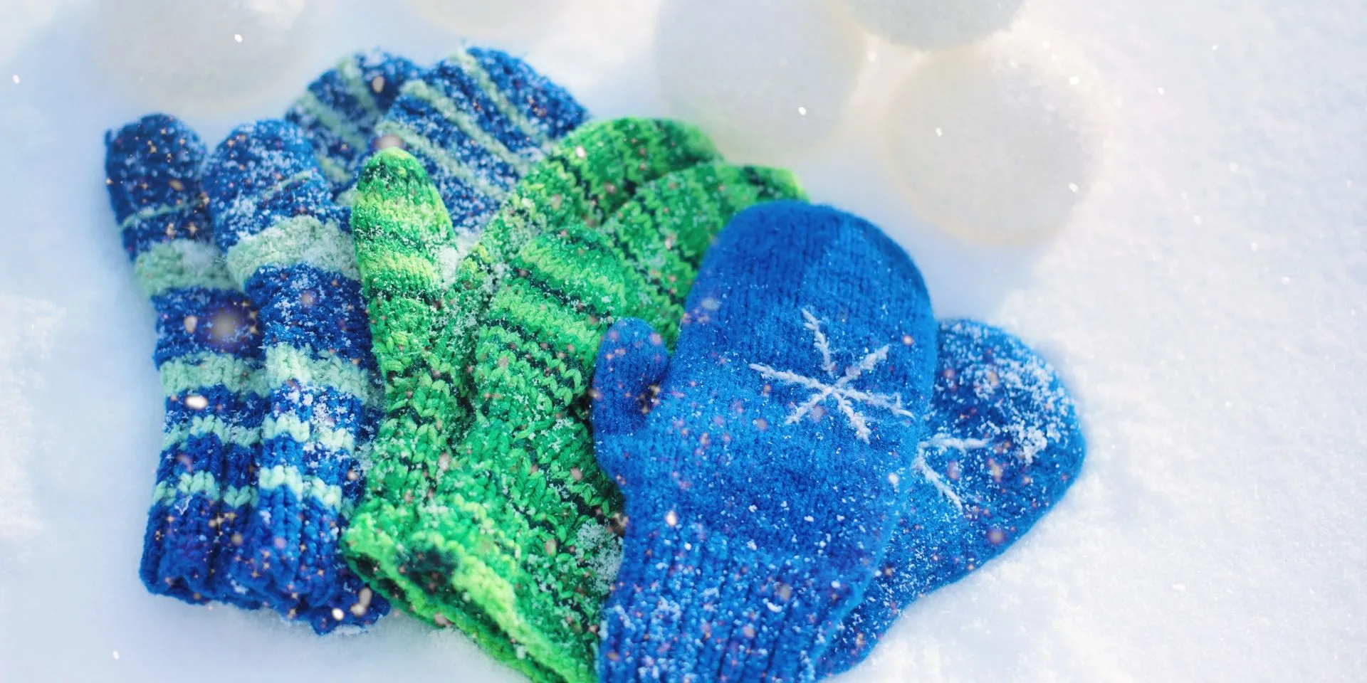 Three pairs of blue and green mittens in the snow