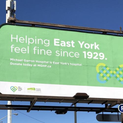Green billboard that reads "Helping East York feel fine since 1929. Michael Garron Hospital is East York's hospital. Donate today at MGHF.ca"