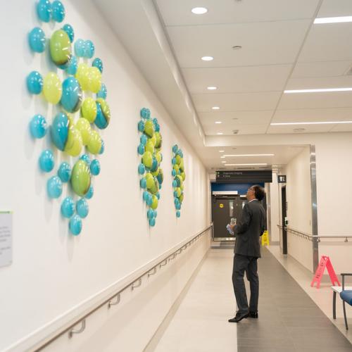 person standing in hallway admiring a wall filled with hand blown glass orbs engraved with donor names.