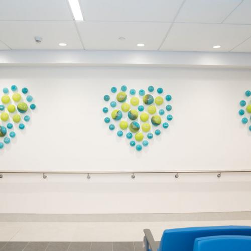 a wall with blue and green glass orbs making up three hearts on the wall, engraved with donor names. 
