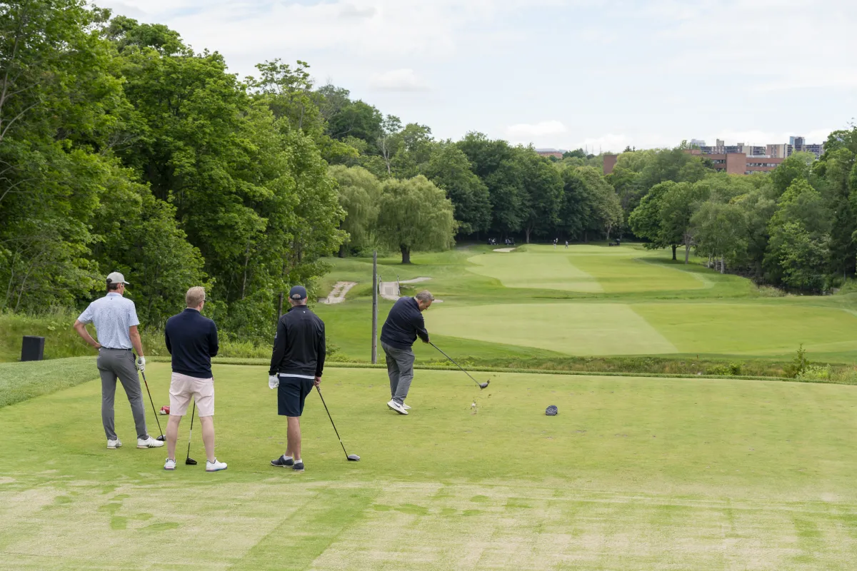 Four men on a golf course, with lush trees around the green