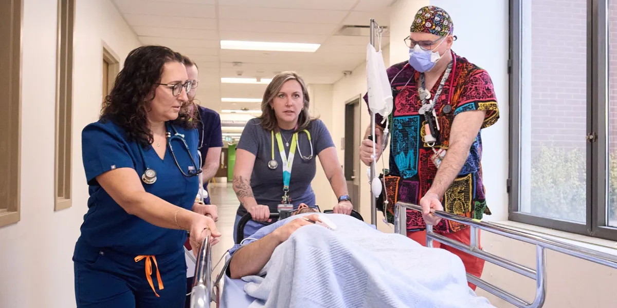 A medical team takes a patient in a bed down a hallway