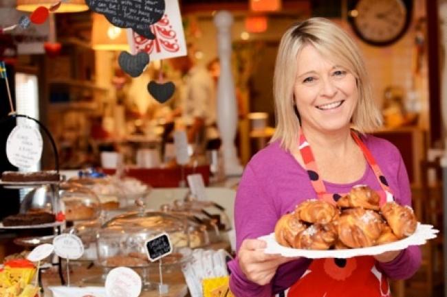 young blonde woman holding a plate of pastries with bakeshop in the background