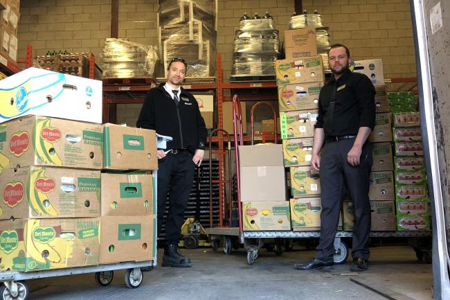 two men standing in back of truck with skids of boxes with food donations 