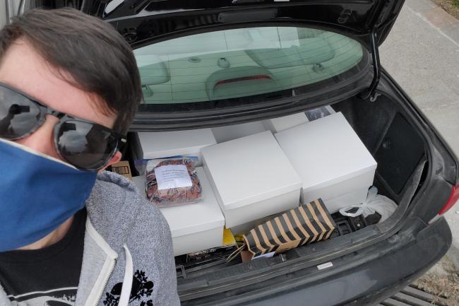 man wearing mask next to car trunk with boxes