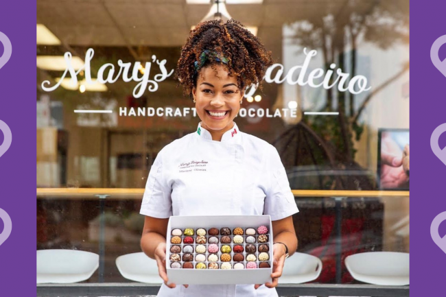 Mary Brigadeiro holding a box of chocolates in front of her chocolate store with a message saying "share the heart this valentine's day"