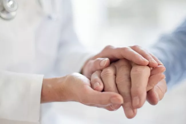 A close up of a physician and patient holding hands