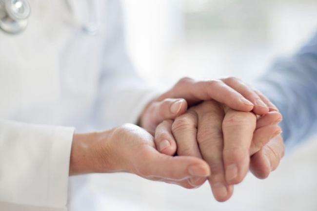 A close up of a physician and patient holding hands