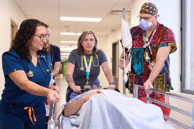 A medical team takes a patient in a bed down a hallway