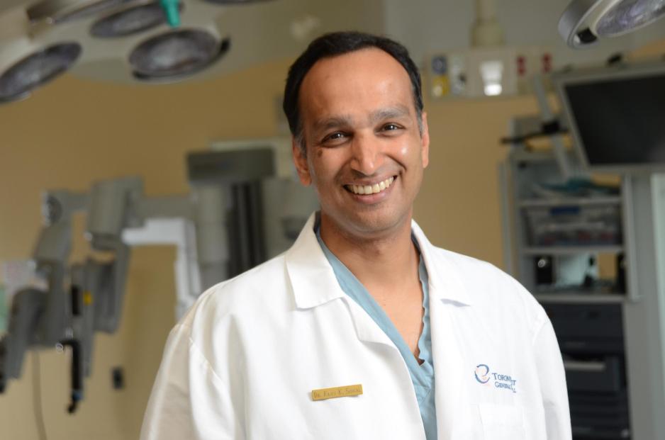 Photo of Dr Signal in his white lab coat in an operating room, smiling at the camera